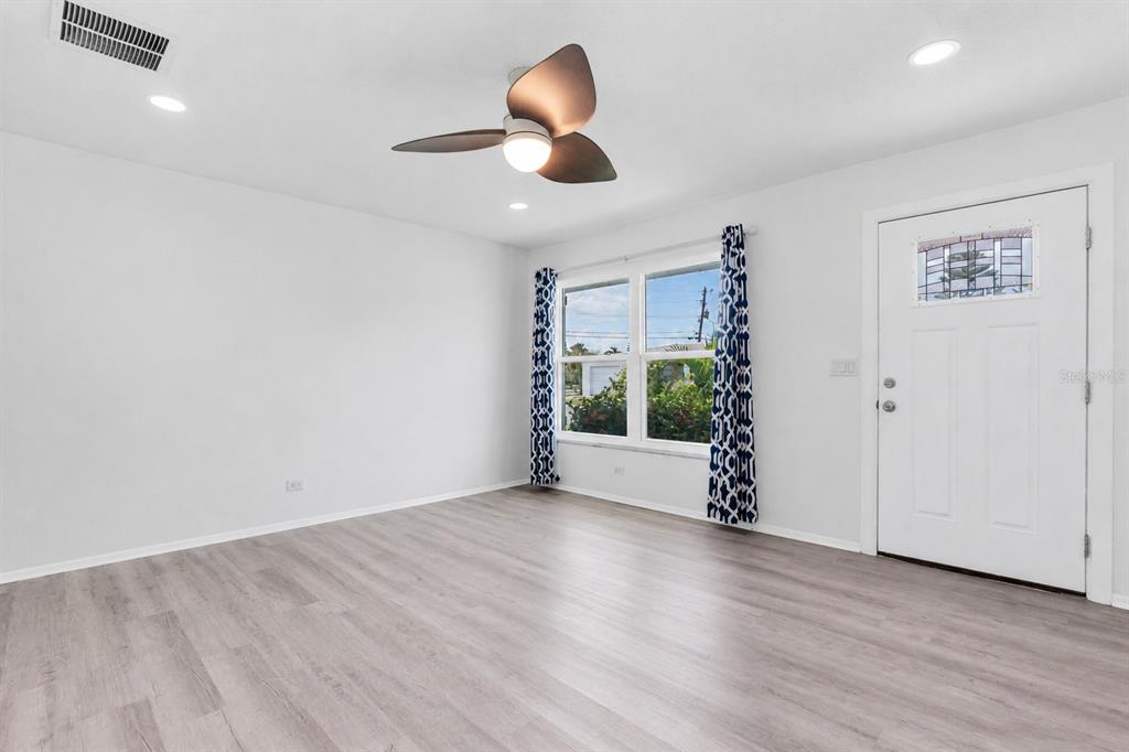 A bright living room features light wood-look flooring, a ceiling fan, and a white door — 3715 98TH AVENUE N UNIT 3, PINELLAS PARK, FL