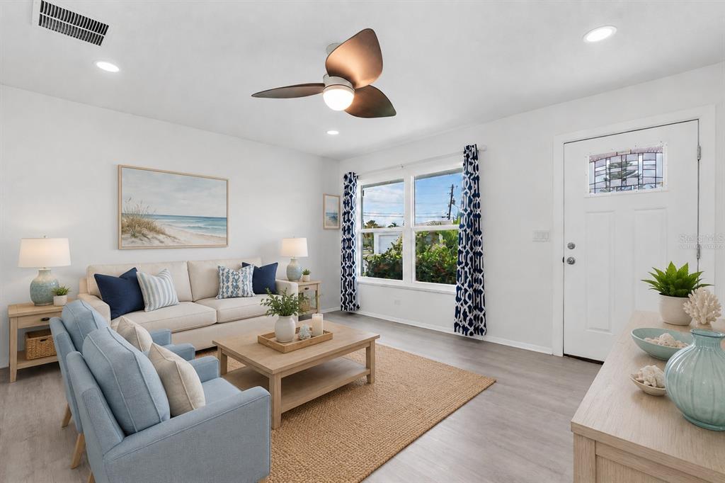 A living room features light wood flooring, a beige sofa, blue armchairs, and a ceiling fan — 3715 98TH AVENUE N UNIT 3, PINELLAS PARK, FL