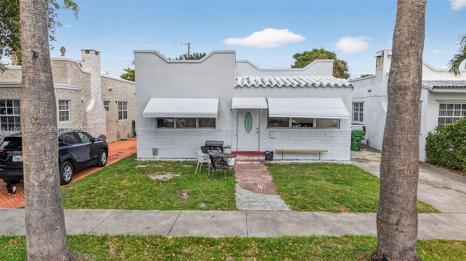 A single-story white house with a flat roof and metal awnings sits behind a lawn — 623 NE 4th St, Hallandale Beach FL 33009, HALLANDALE BEACH, FL
