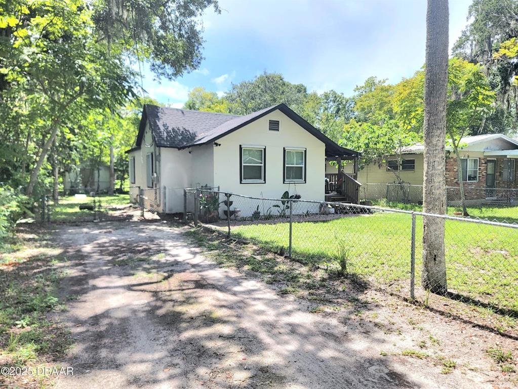 A single-story house with a light-colored exterior and a dark roof sits behind a fence — 620 WASHINGTON STREET, DAYTONA BEACH, FL