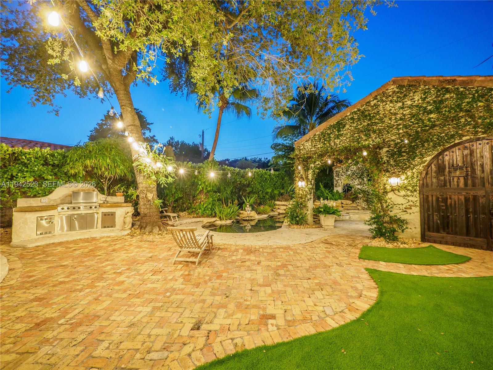 A backyard patio features a brick floor, outdoor kitchen, small pond, and string lights — 1229 Sorolla Ave, Coral Gables FL 33134, CORAL GABLES, FL