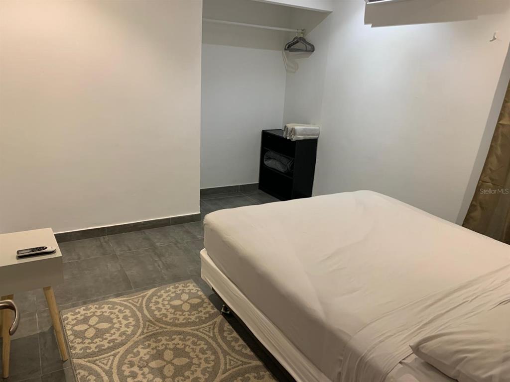 A bedroom features a bed, a small nightstand, a patterned rug, and a closet area — Atlantic View ISLA VERDE, CAROLINA, PR