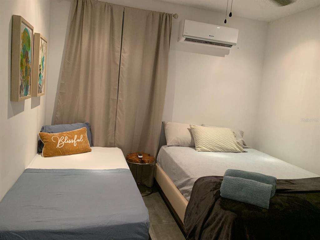 A bedroom contains two beds, a small side table, wall art, and a wall-mounted air conditioner — Atlantic View ISLA VERDE, CAROLINA, PR