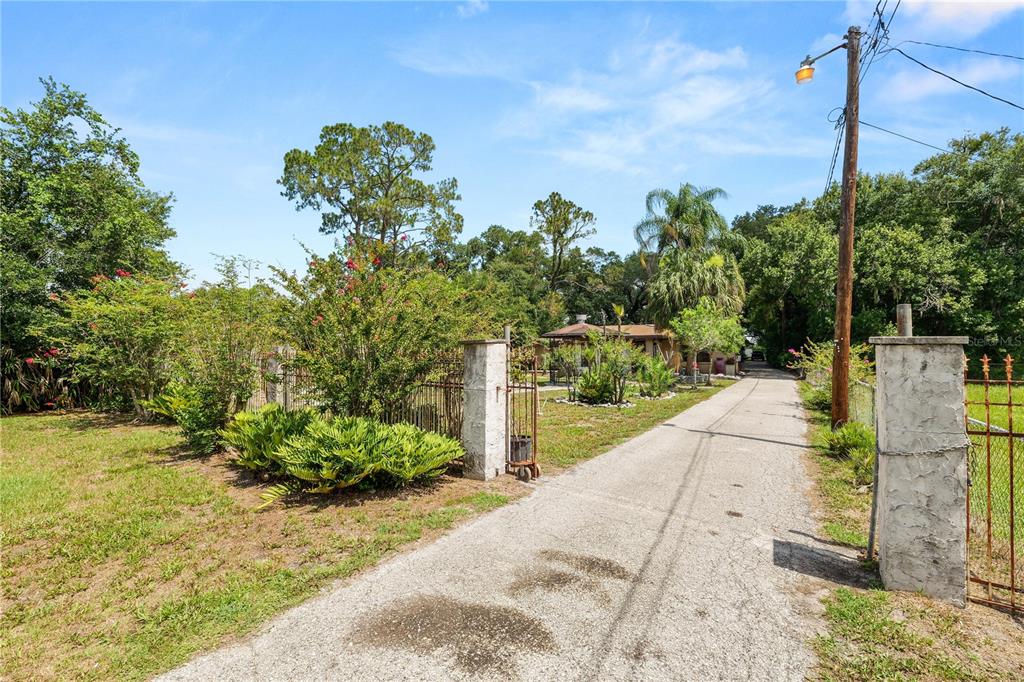 A paved driveway leads through a gated entrance toward a house surrounded by trees — 4125 SWINDELL ROAD, LAKELAND, FL