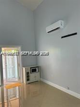 A room with light-colored walls, tile flooring, a wall-mounted air conditioner, and a small cabinet — 16870 SW 142nd Pl # 1, Miami FL 33177, MIAMI, FL