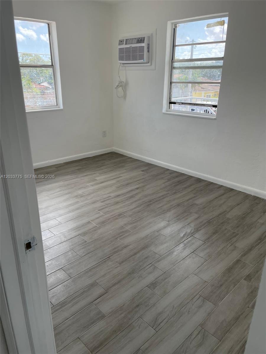An empty room features white walls, wood-look tile flooring, two windows, and a wall-mounted air conditioner — 1261 NW 59th St # 14, Miami FL 33142, MIAMI, FL