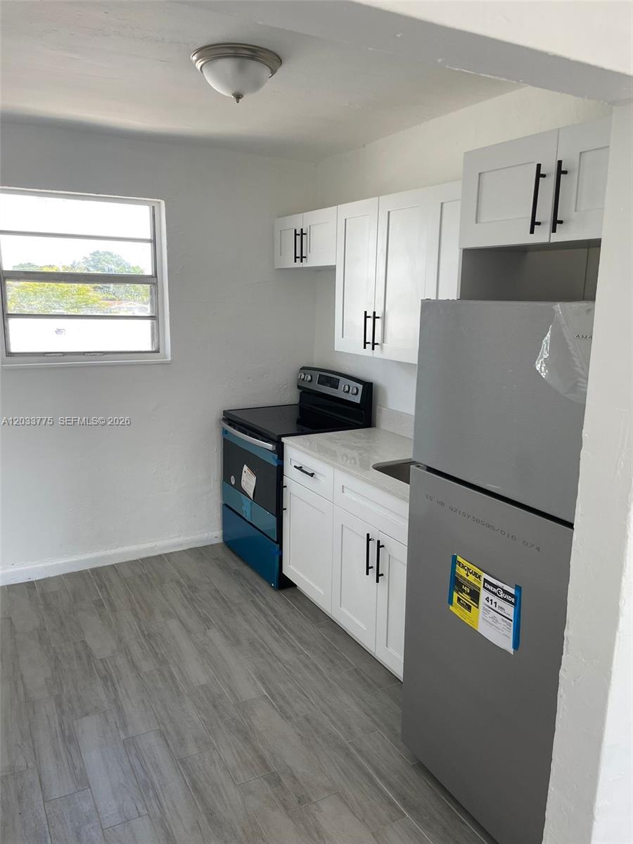 A small kitchen features white cabinets, stainless steel appliances, and light gray wood-look flooring — 1261 NW 59th St # 14, Miami FL 33142, MIAMI, FL