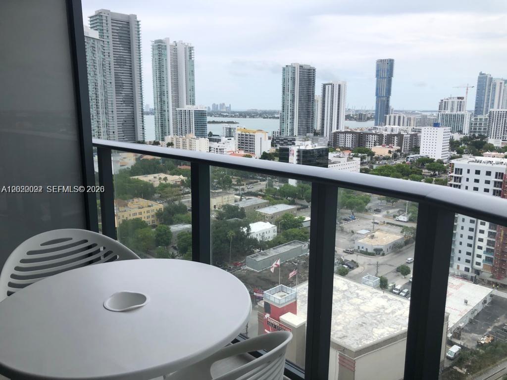 A balcony with a small white table and chairs overlooks a dense city skyline — 121 NE 34th St # 2203, Miami FL 33137, MIAMI, FL