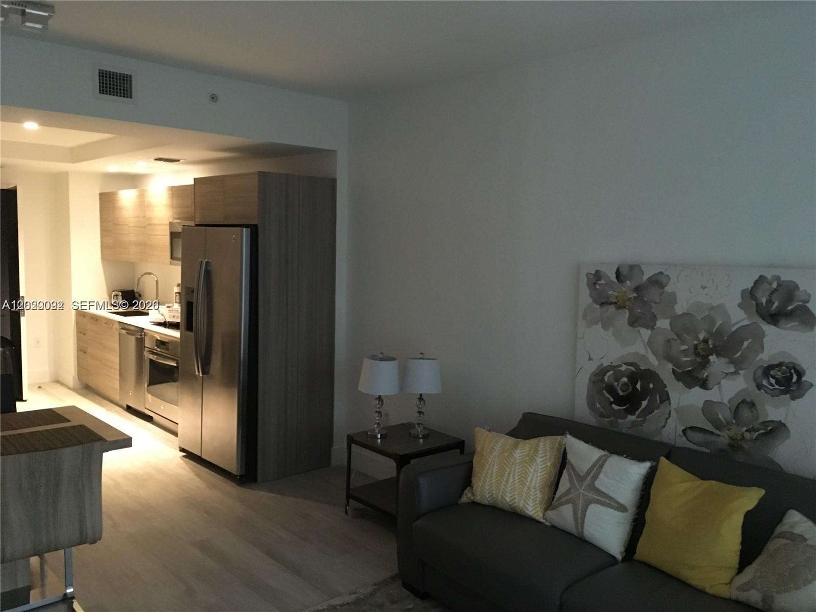 A living room with a gray sofa and a kitchen featuring stainless steel appliances — 121 NE 34th St # 2203, Miami FL 33137, MIAMI, FL