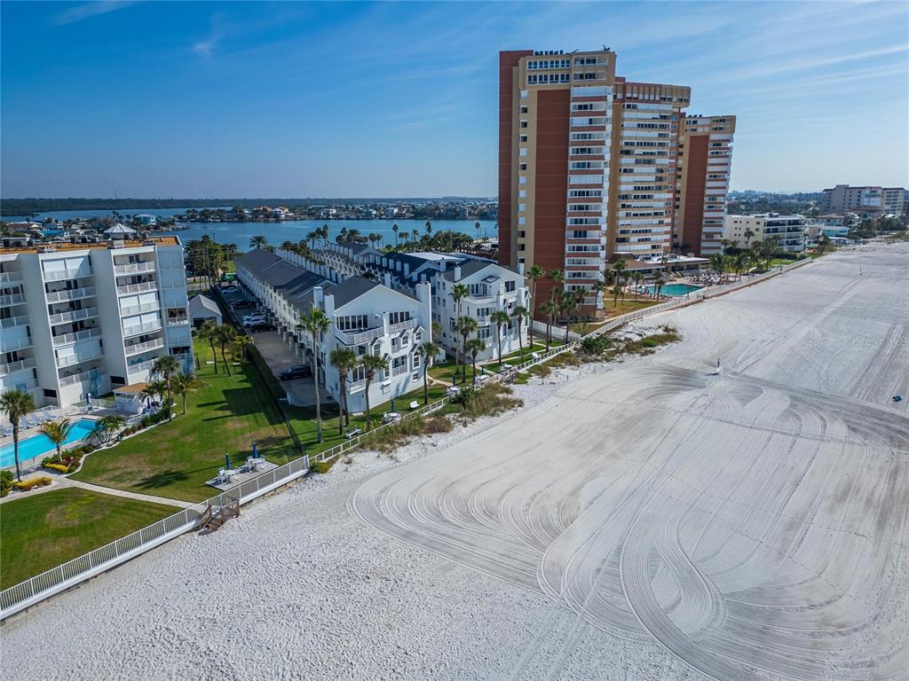 An aerial view shows a sandy beach, residential townhomes, and a tall beachfront condominium building — 17960 GULF BOULEVARD UNIT 104, REDINGTON SHORES, FL