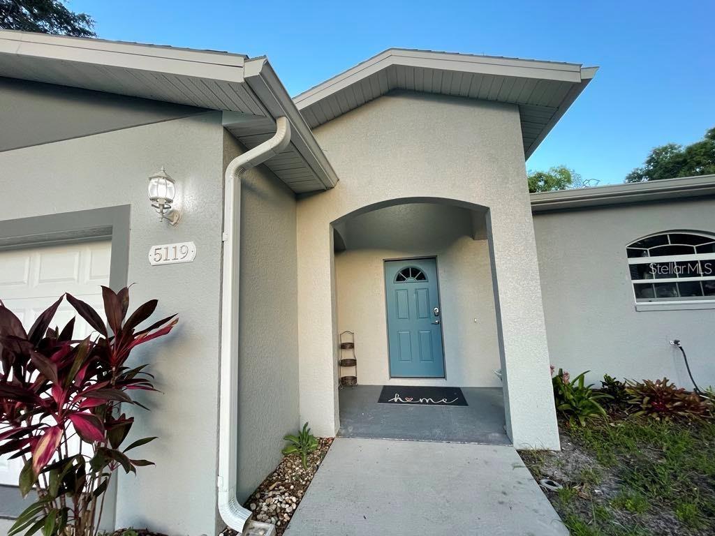 The exterior of a house features a light blue front door and a concrete walkway — 5119 RILMA AVENUE, SARASOTA, FL