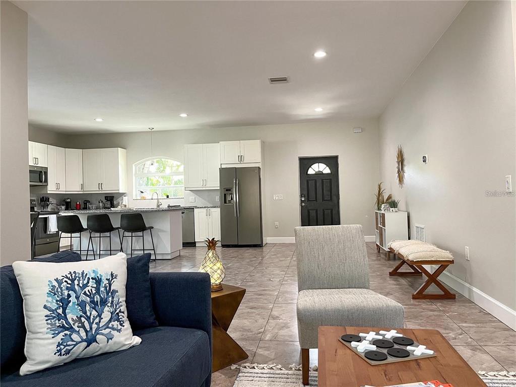 A modern open-concept kitchen and living area features white cabinetry, tile flooring, and neutral walls — 5119 RILMA AVENUE, SARASOTA, FL