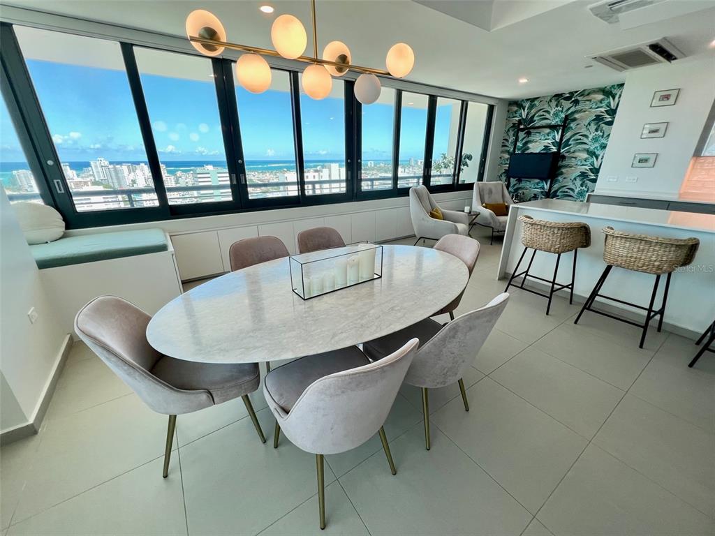 A dining area features an oval marble table, upholstered chairs, and floor-to-ceiling ocean view windows — 1511 22 PONCE DE LEON AVE. UNIT 9151, SAN JUAN, PR