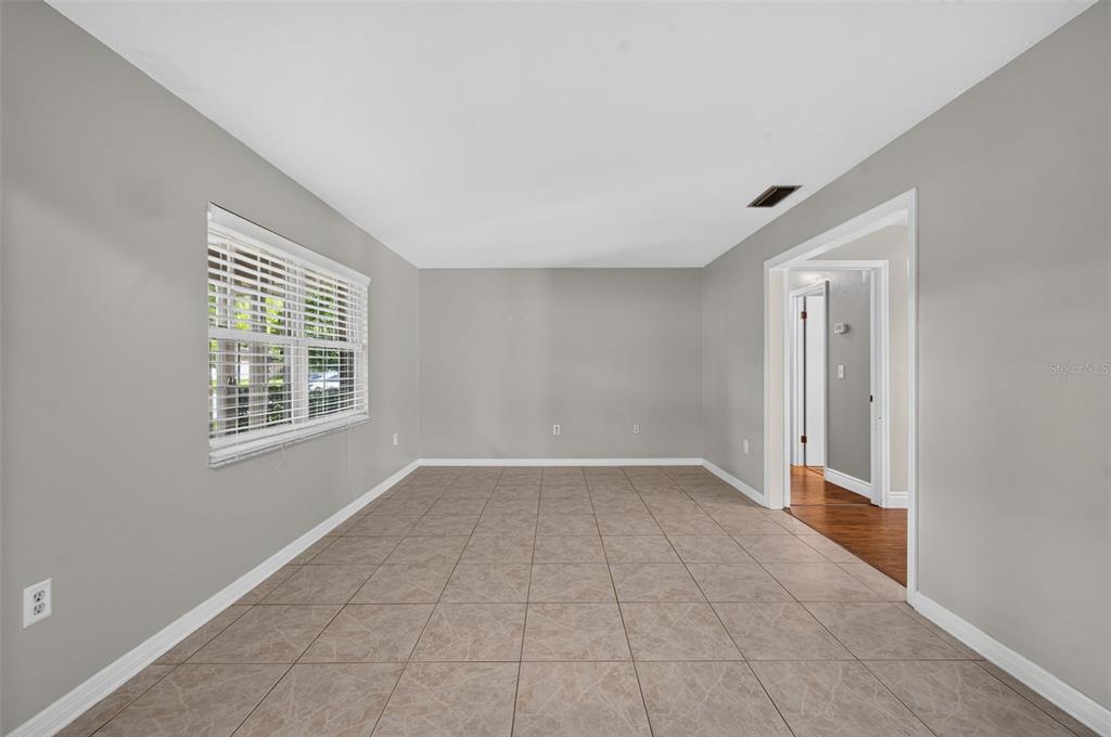 An empty room features light gray walls, large beige floor tiles, and a white window — 3240 TOURAINE AVENUE, ORLANDO, FL