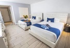 A hotel room features two beds with white headboards, blue runners, and light wood-look tile flooring — 7310 Harding Ave # 1, Miami Beach FL 33141, MIAMI BEACH, FL