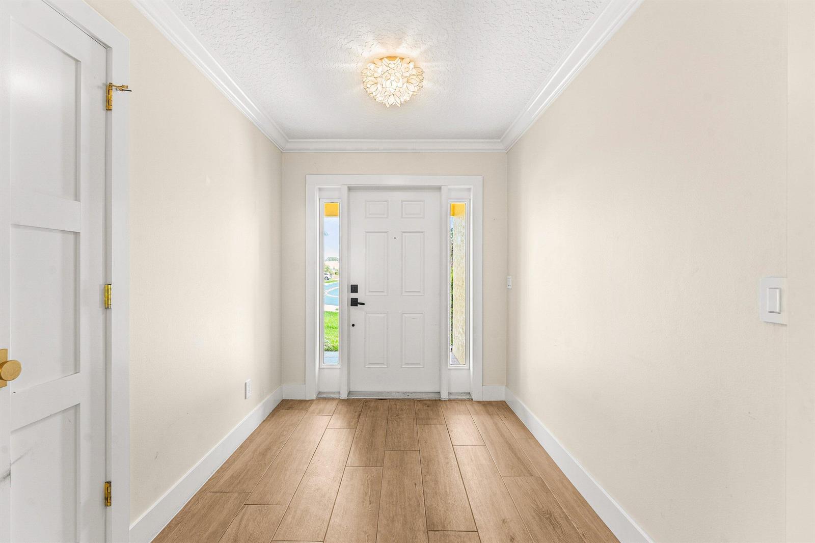 A bright entryway features light wood-look flooring, a white front door with sidelights, and crown molding — 226 Moccasin Trail W, Jupiter FL 33458, JUPITER, FL