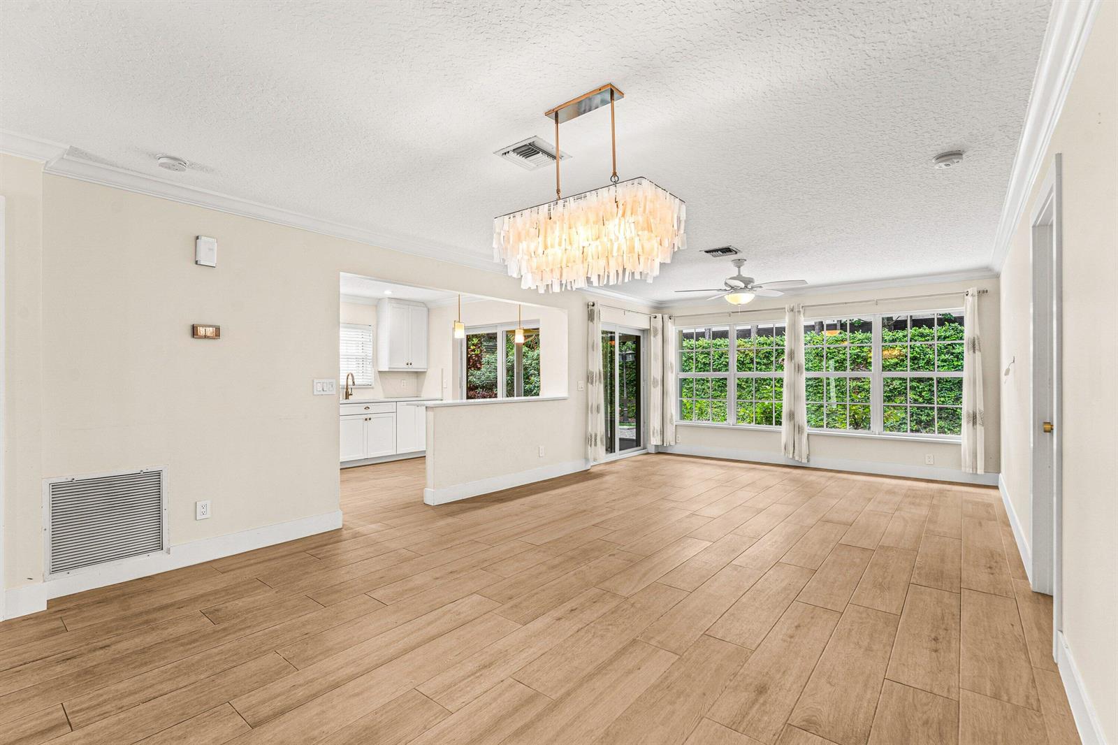 An open-concept living area features light wood-look tile floors, a chandelier, and a kitchen pass-through — 226 Moccasin Trail W, Jupiter FL 33458, JUPITER, FL