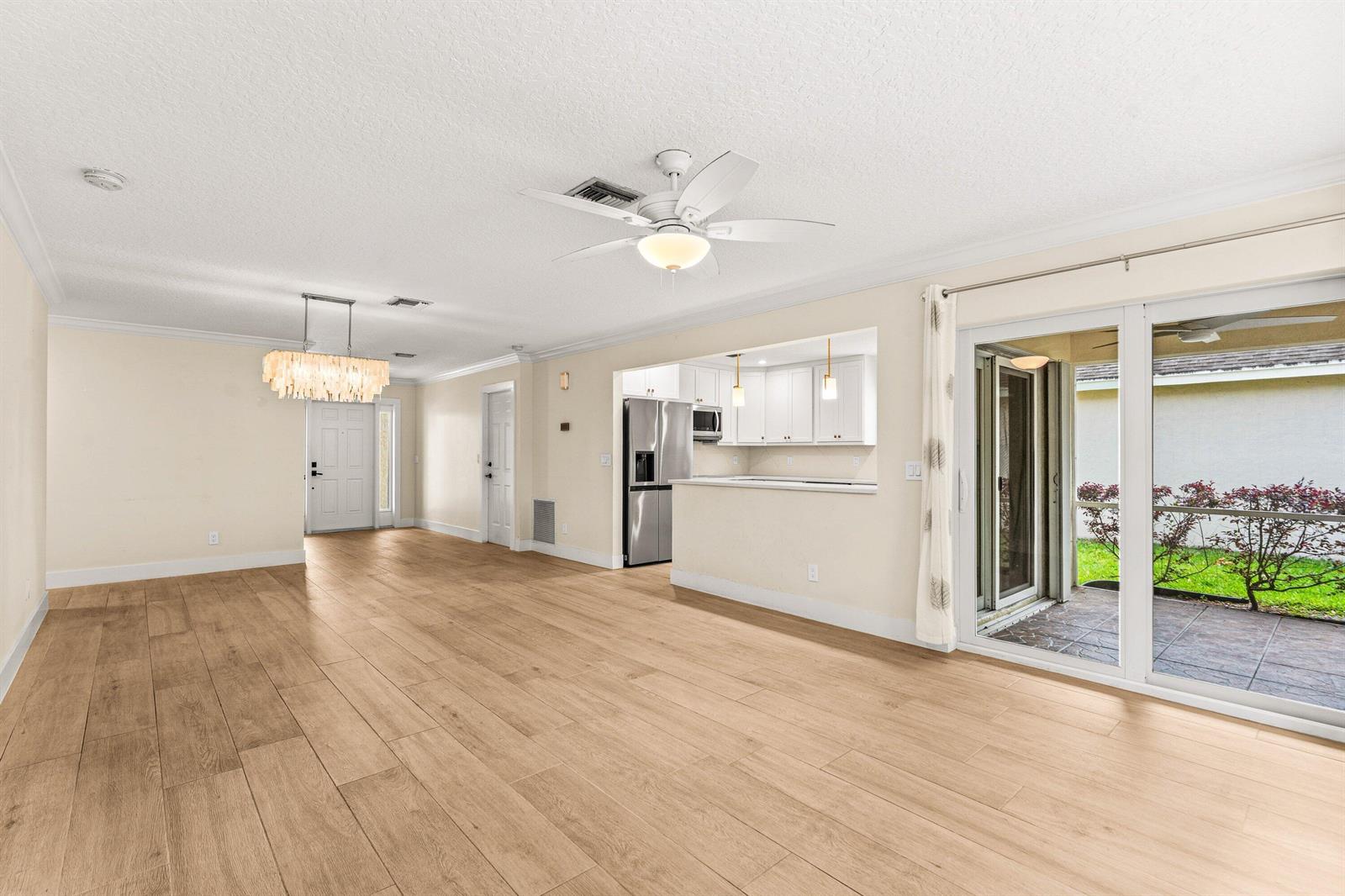 An open-concept living area features light wood-look tile flooring, a ceiling fan, and a kitchen — 226 Moccasin Trail W, Jupiter FL 33458, JUPITER, FL