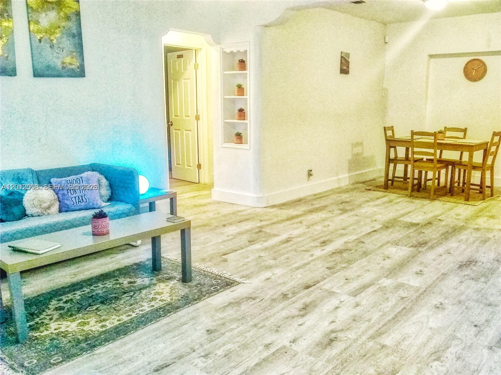A living and dining area features light wood-look flooring, a blue sofa, and built-in shelving — 142 NE 56th St # A, Miami FL 33137, MIAMI, FL