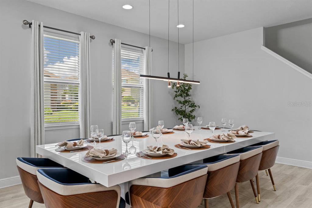 A dining room features a long white table, modern chairs, and a linear pendant light — 451 BURMA STREET, KISSIMMEE, FL