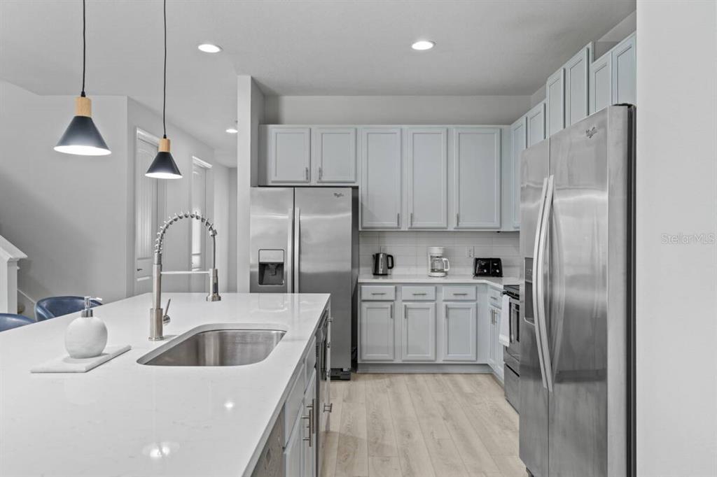 A modern kitchen features light gray cabinets, stainless steel appliances, and a white quartz island — 451 BURMA STREET, KISSIMMEE, FL
