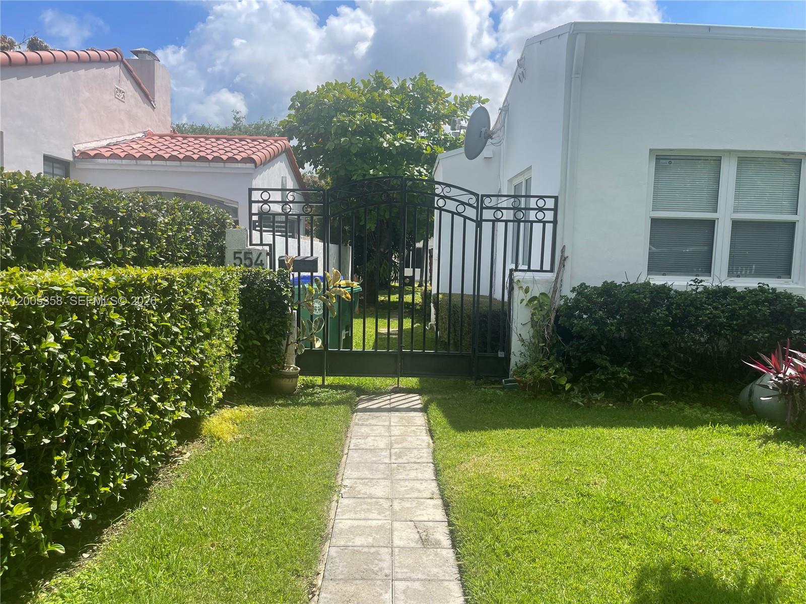 A paved walkway leads to a black metal gate between two white residential buildings — 554 NE 74th St # 2, Miami FL 33138, MIAMI, FL