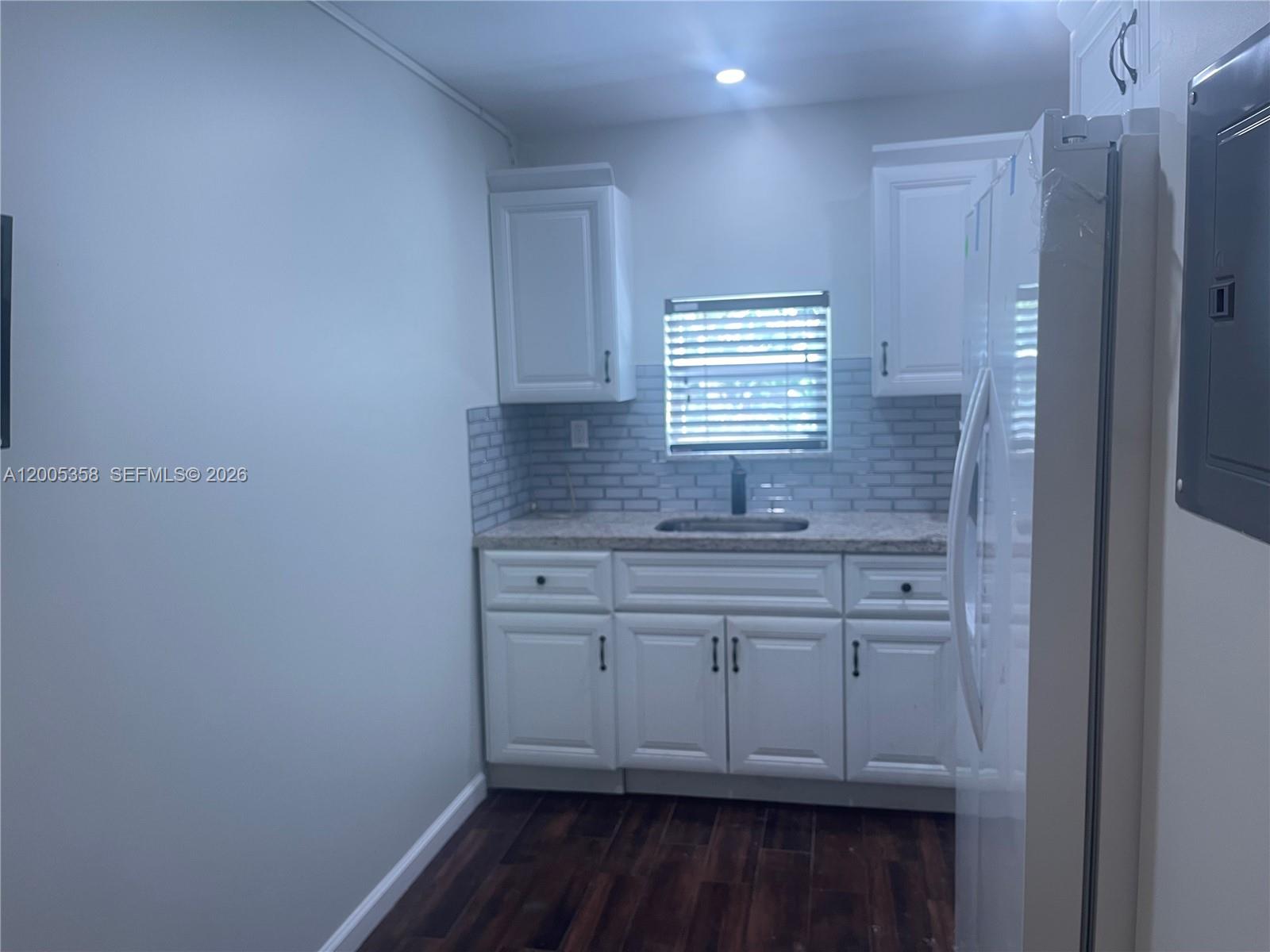 A small kitchen features white cabinets, a gray subway tile backsplash, and dark wood flooring — 554 NE 74th St # 2, Miami FL 33138, MIAMI, FL