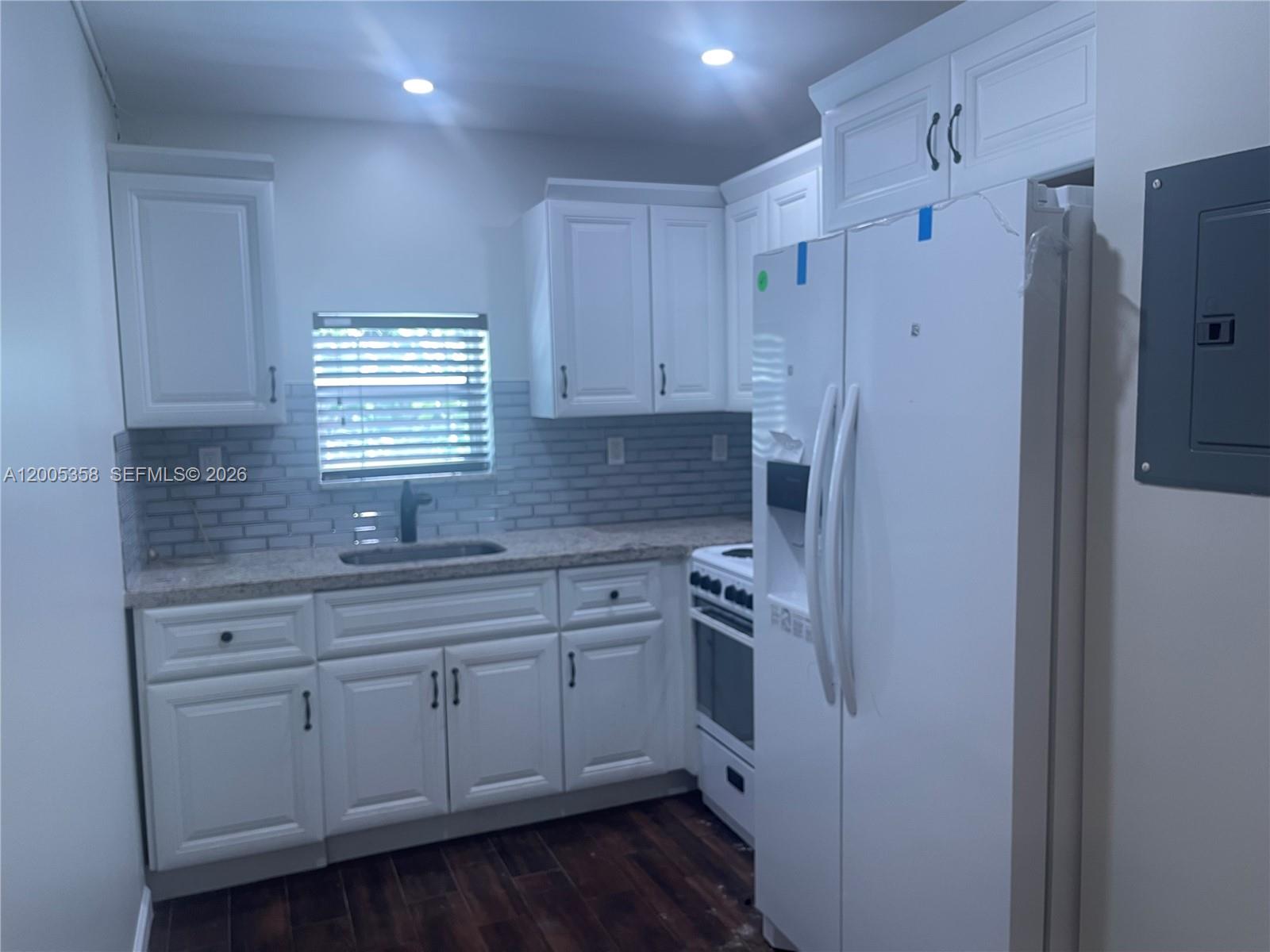 A kitchen features white cabinets, a granite countertop, a subway tile backsplash, and white appliances — 554 NE 74th St # 2, Miami FL 33138, MIAMI, FL