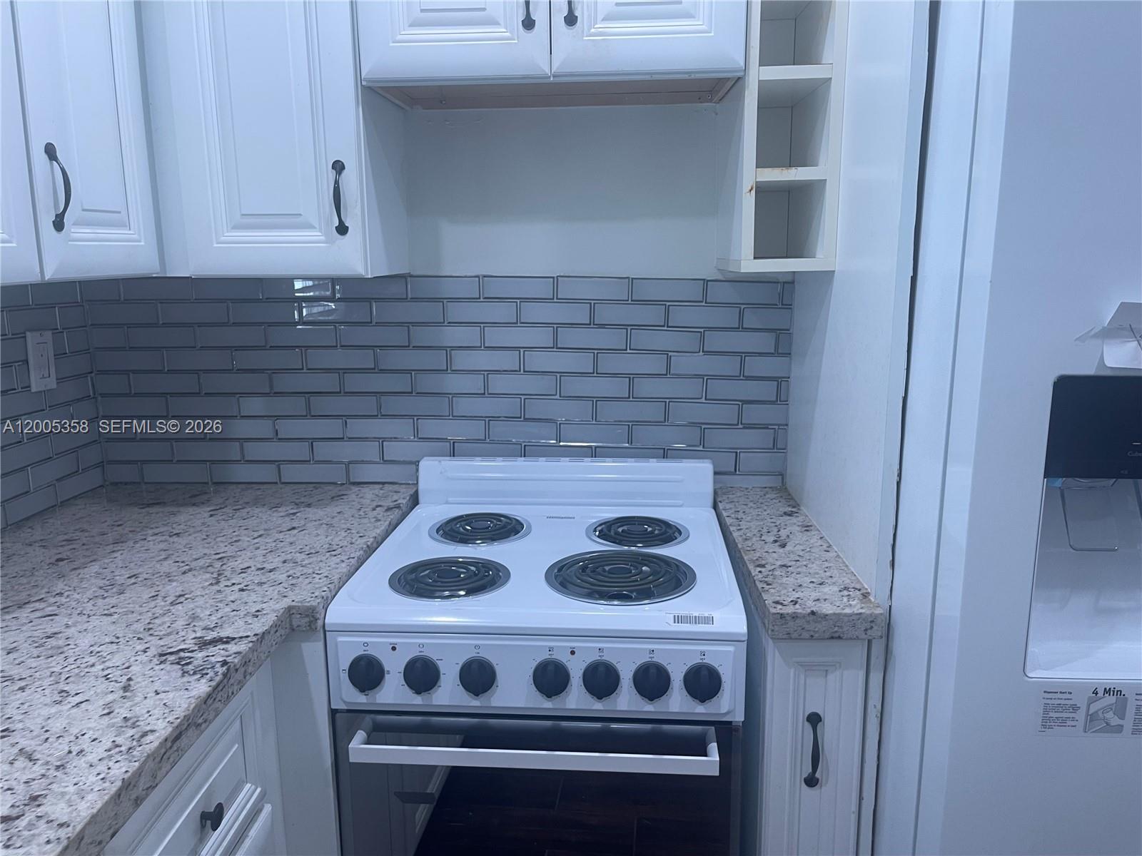 A kitchen features white cabinets, a white electric stove, and a gray subway tile backsplash — 554 NE 74th St # 2, Miami FL 33138, MIAMI, FL