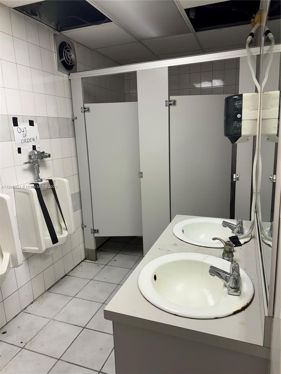 A public restroom features white tiled walls, two sinks, and a urinal marked out of order — 12495 NE 2nd Ave, North Miami FL 33161, NORTH MIAMI, FL