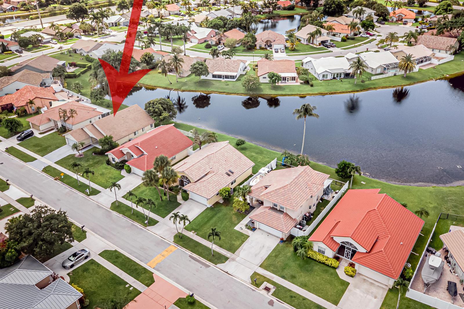 An aerial view shows a suburban neighborhood with houses featuring red-tiled roofs near a lake — 5148 Rosen Boulevard, Boynton Beach FL 33472, BOYNTON BEACH, FL