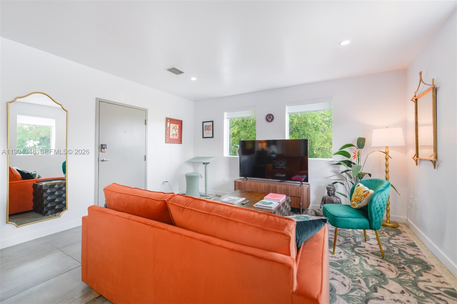 A living room features an orange sofa, a green armchair, and a television on a stand — 165 NW 39th St # 7, Miami FL 33127, MIAMI, FL