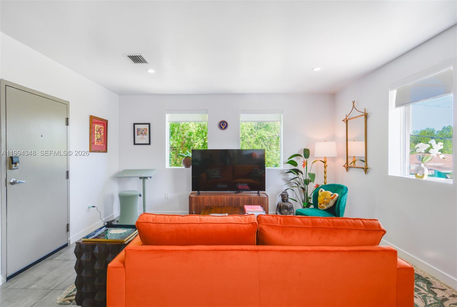 A living room features an orange sofa, a television on a console, and two windows — 165 NW 39th St # 7, Miami FL 33127, MIAMI, FL