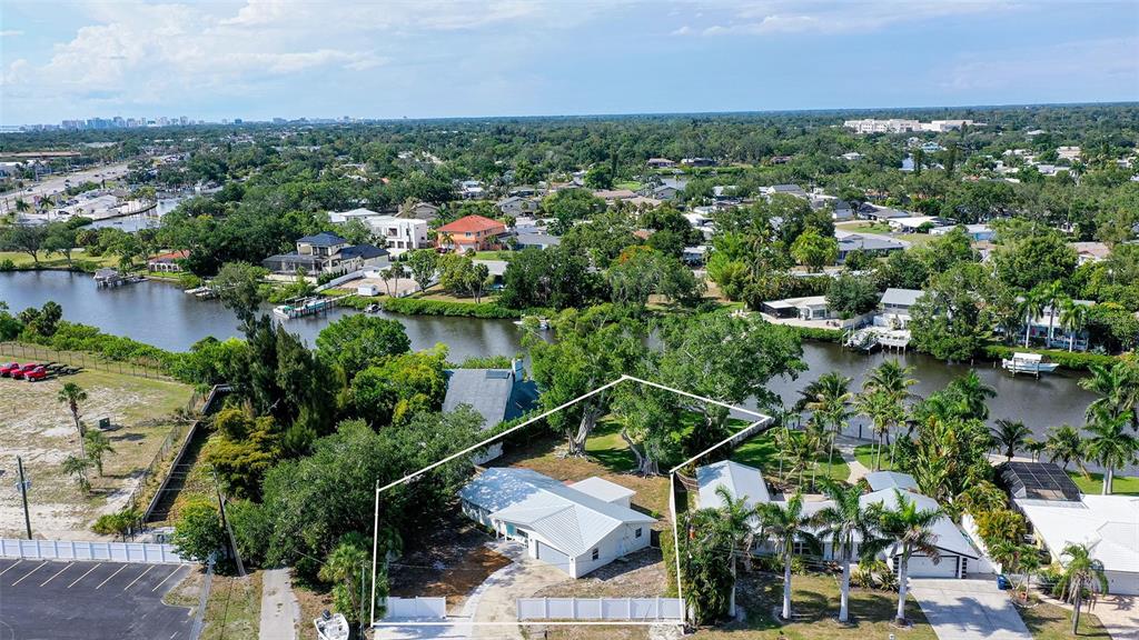 An aerial view shows a single-story house with a white roof situated along a canal — 2103 LUSITANIA DRIVE, SARASOTA, FL