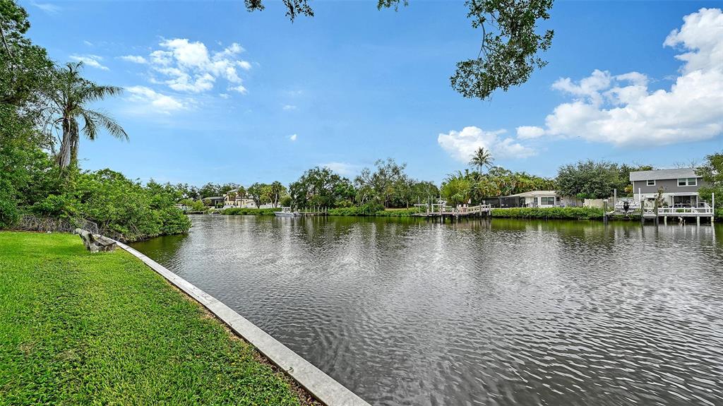 A grassy lawn borders a canal with boat docks and houses in the background — 2103 LUSITANIA DRIVE, SARASOTA, FL