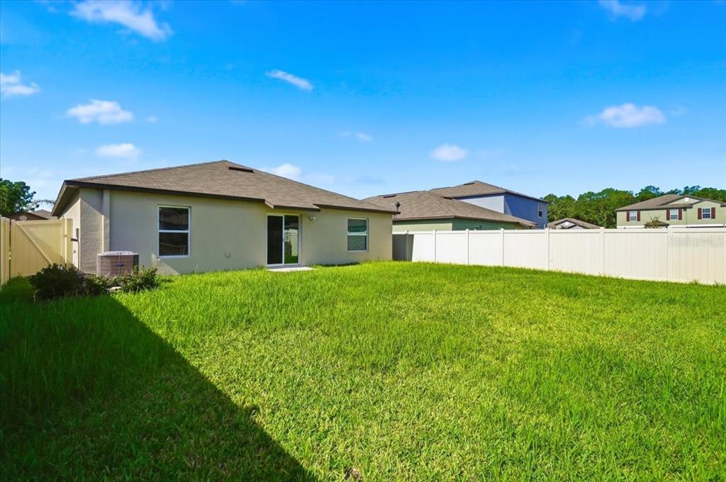 The backyard of a single-story house features a grassy lawn and a white vinyl fence — 4316 TROTTERS WAY, LAKELAND, FL