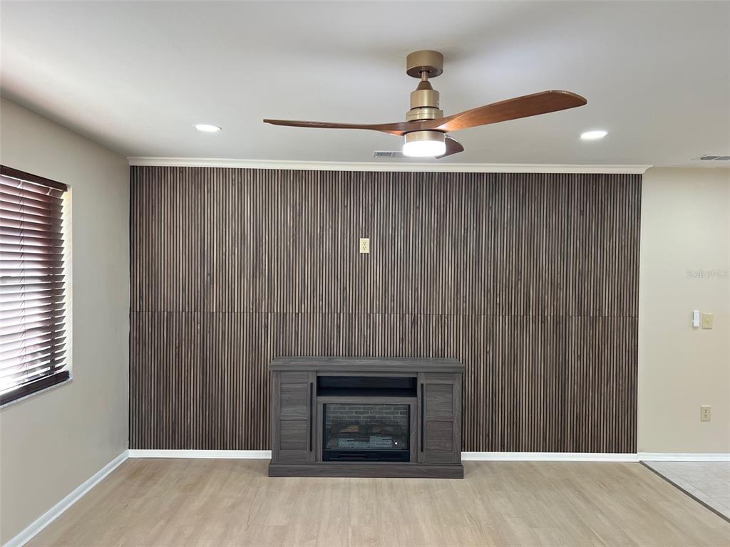 A living room features a wood-slat accent wall, a fireplace console, and a ceiling fan — 5970 80TH STREET N UNIT 101, ST PETERSBURG, FL
