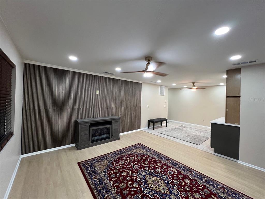 A living room features light wood flooring, a slatted wood accent wall, and two ceiling fans — 5970 80TH STREET N UNIT 101, ST PETERSBURG, FL