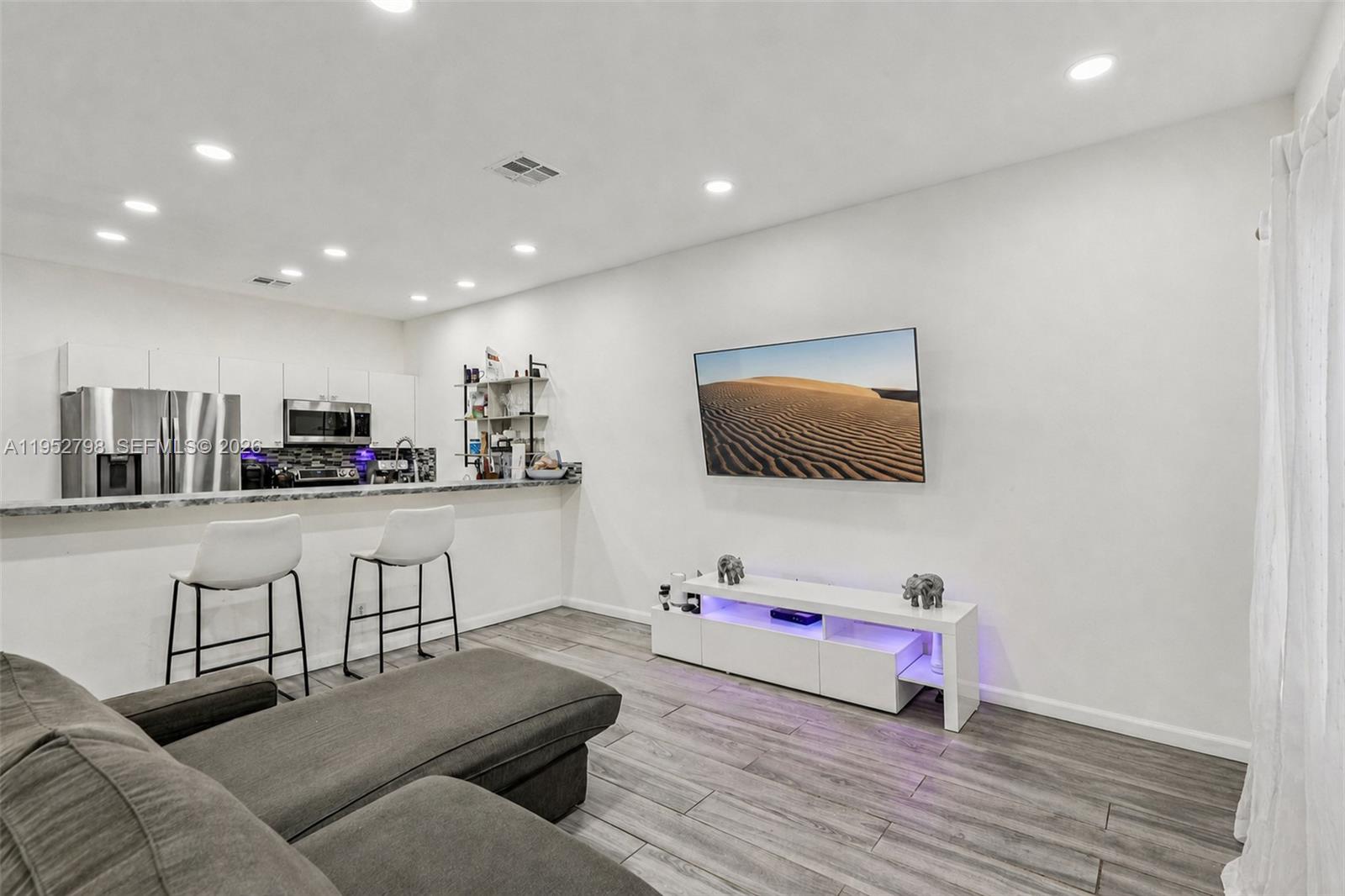 A living room with a kitchen bar, gray sectional sofa, and wall-mounted television — 2307 Washington St # 5, Hollywood FL 33020, HOLLYWOOD, FL