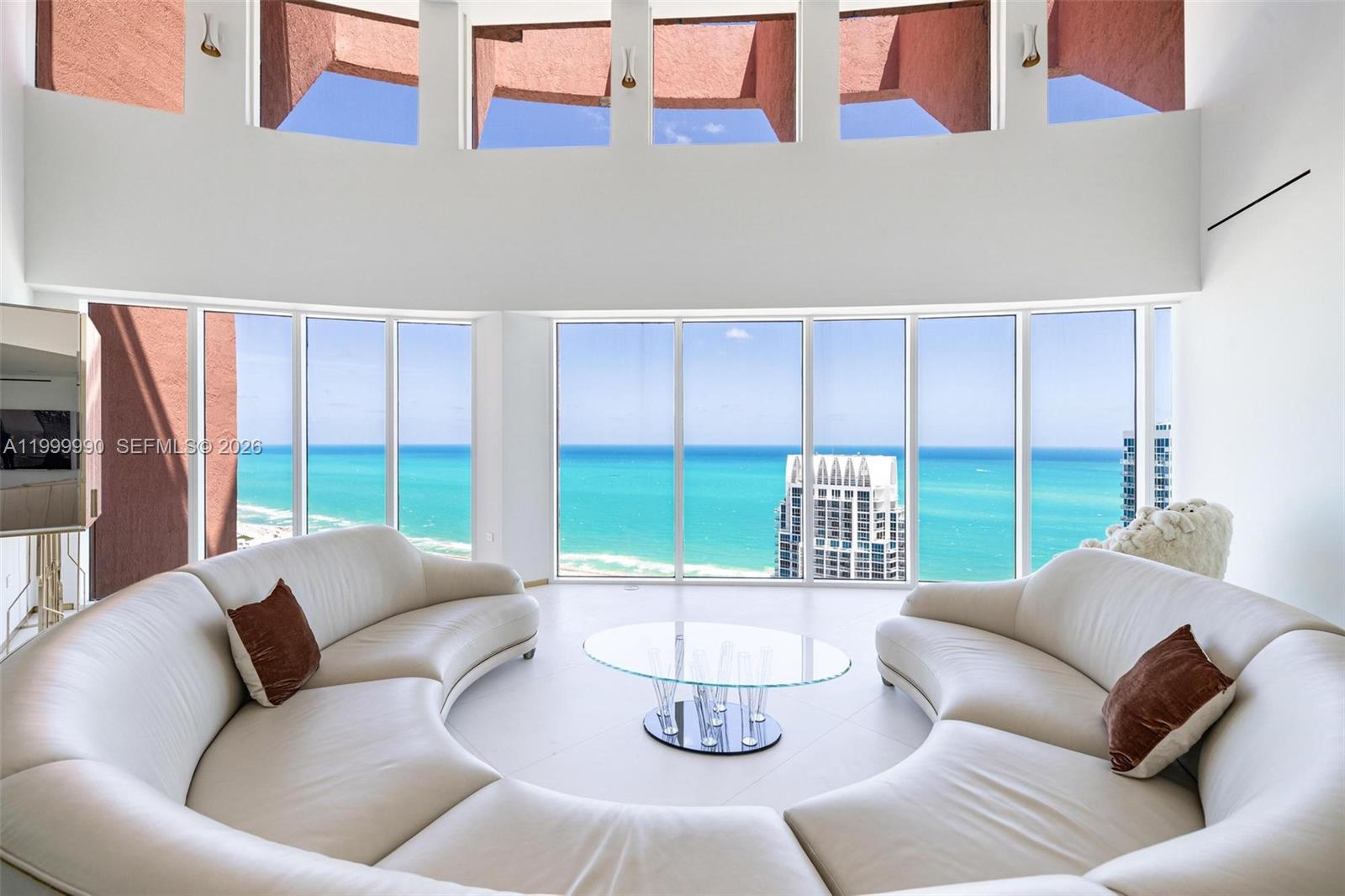 A living room features two curved white sofas, a glass coffee table, and floor-to-ceiling ocean views — 300 S Pointe Dr # 5, Miami Beach FL 33139, MIAMI BEACH, FL