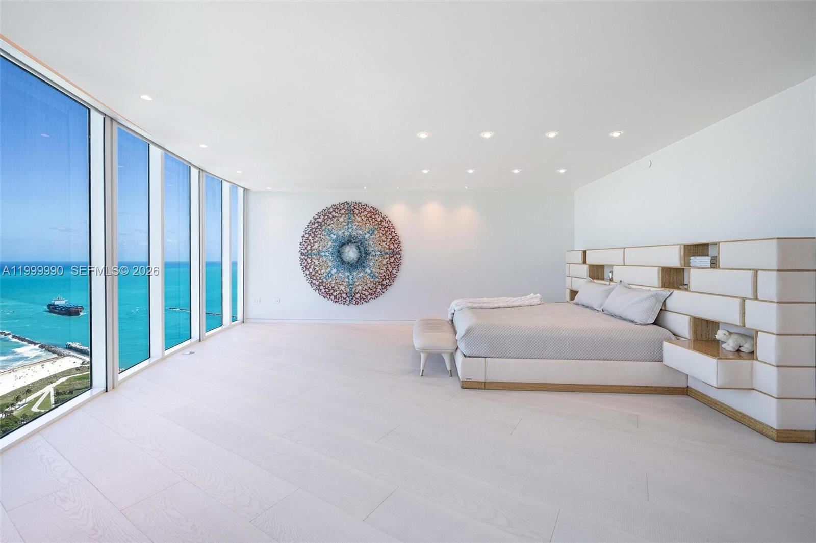 A modern bedroom features floor-to-ceiling windows overlooking the ocean, white flooring, and a large mural — 300 S Pointe Dr # 5, Miami Beach FL 33139, MIAMI BEACH, FL