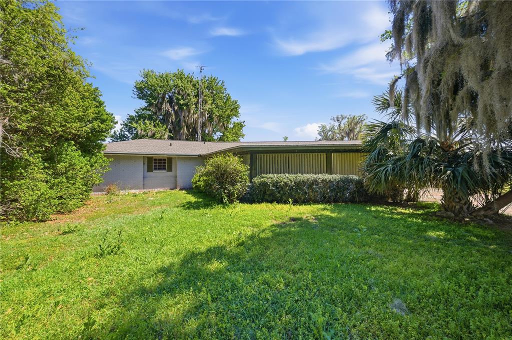 A single-story brick house with a covered porch sits behind a grassy lawn and trees — 21407 NW 39TH COURT, MICANOPY, FL
