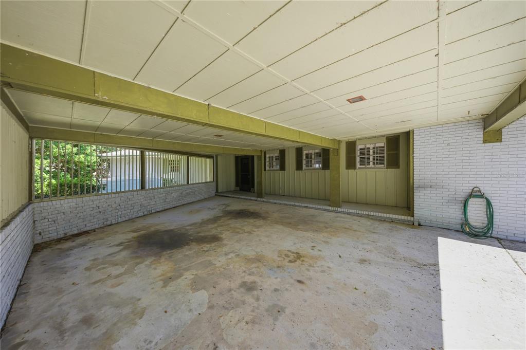 A covered carport with a concrete floor, white brick walls, and a slatted metal screen — 21407 NW 39TH COURT, MICANOPY, FL