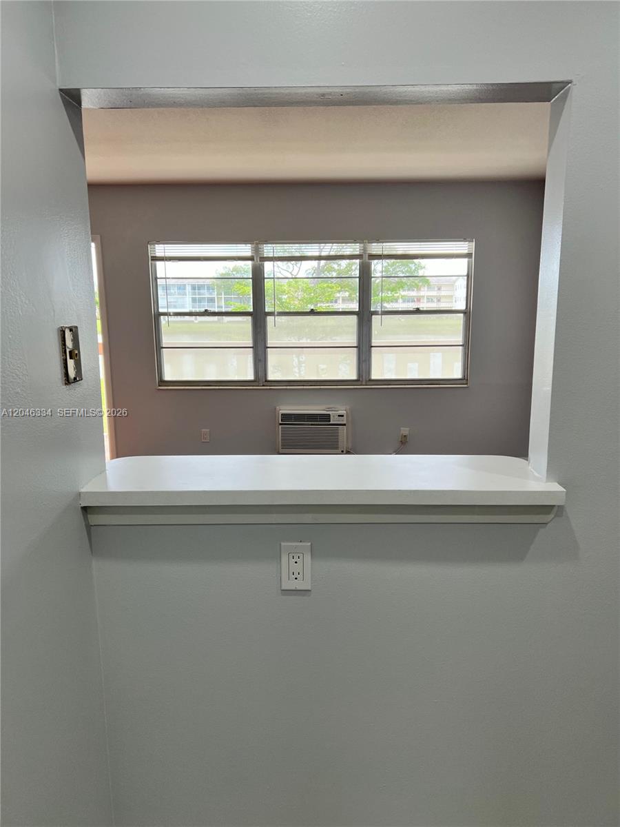 A view through a kitchen pass-through window looks into a room with a window air conditioner — 359 Preston I # I, Boca Raton FL 33434, BOCA RATON, FL