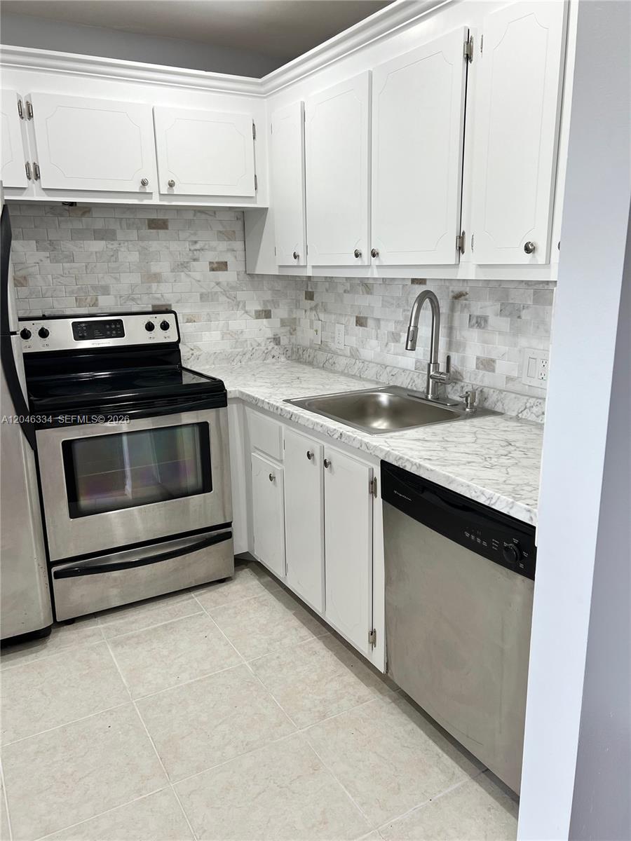 A kitchen features white cabinets, marble-look countertops, a tiled backsplash, and stainless steel appliances — 359 Preston I # I, Boca Raton FL 33434, BOCA RATON, FL