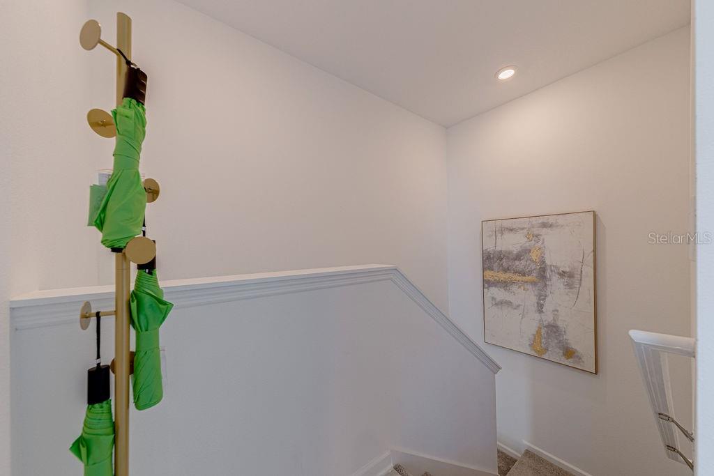 A coat rack with green umbrellas stands near a staircase with white walls and artwork — 9327 SOMMERSET HILLS DRIVE UNIT 9327, DAVENPORT, FL