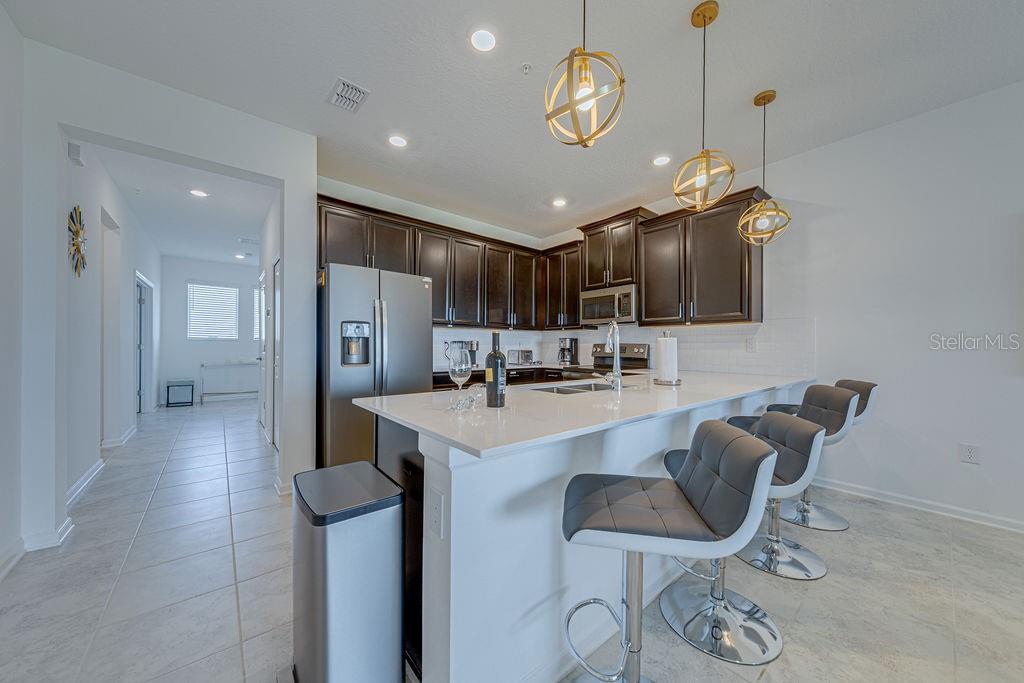 A modern kitchen features dark wood cabinets, white countertops, a breakfast bar, and pendant lighting — 9327 SOMMERSET HILLS DRIVE UNIT 9327, DAVENPORT, FL