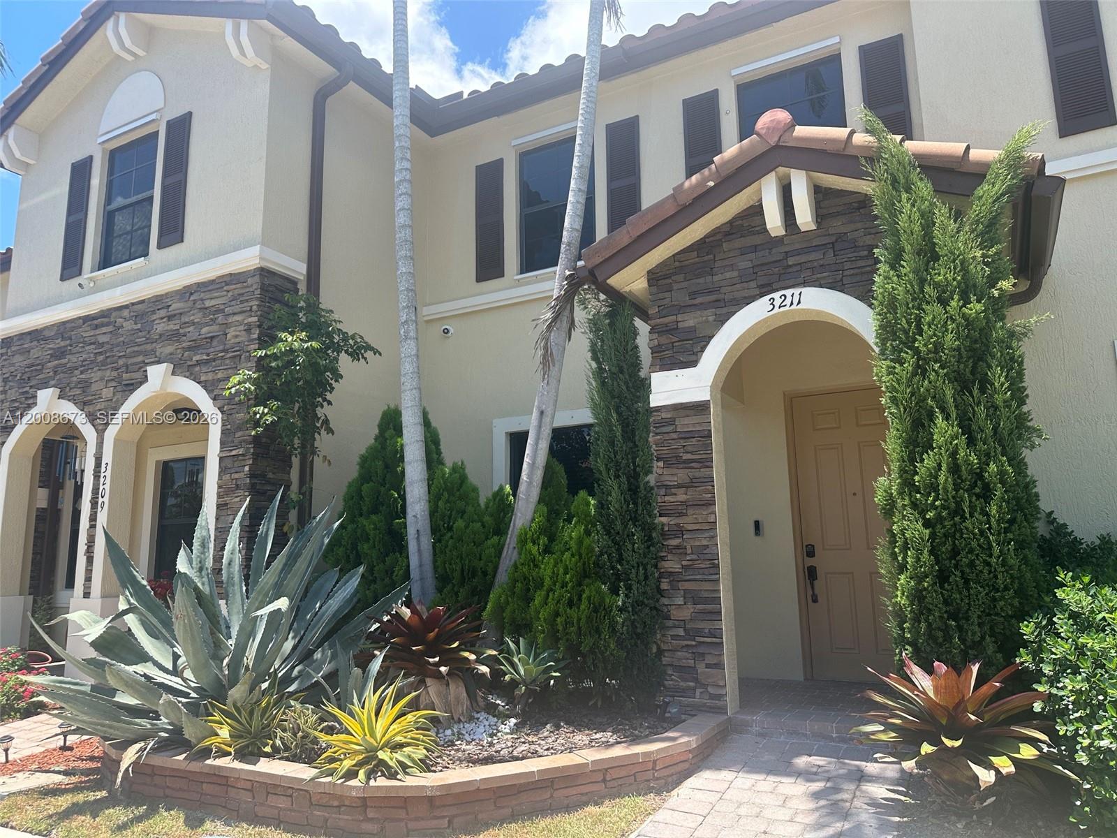 A two-story house exterior features stone veneer accents, arched entryways, and a landscaped front garden — 3211 SE 6th St, Homestead FL 33033, HOMESTEAD, FL
