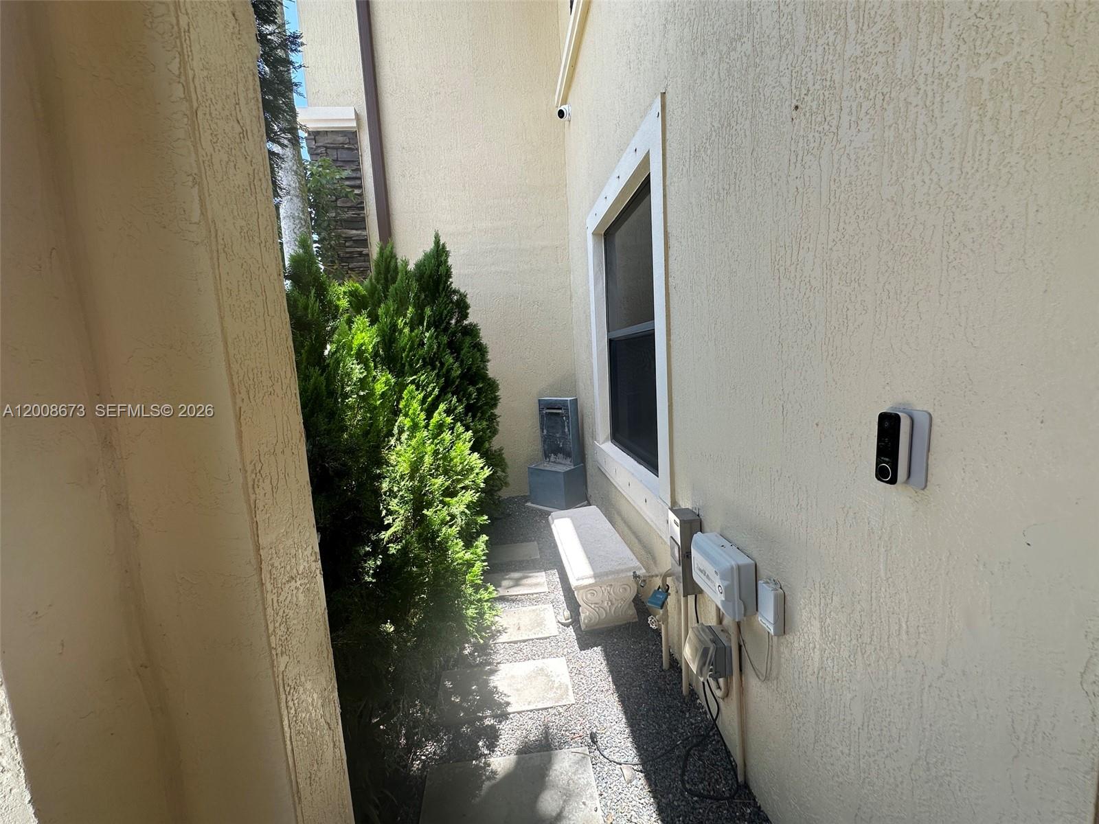 A narrow exterior side yard features a stone path, a small bench, and utility equipment — 3211 SE 6th St, Homestead FL 33033, HOMESTEAD, FL