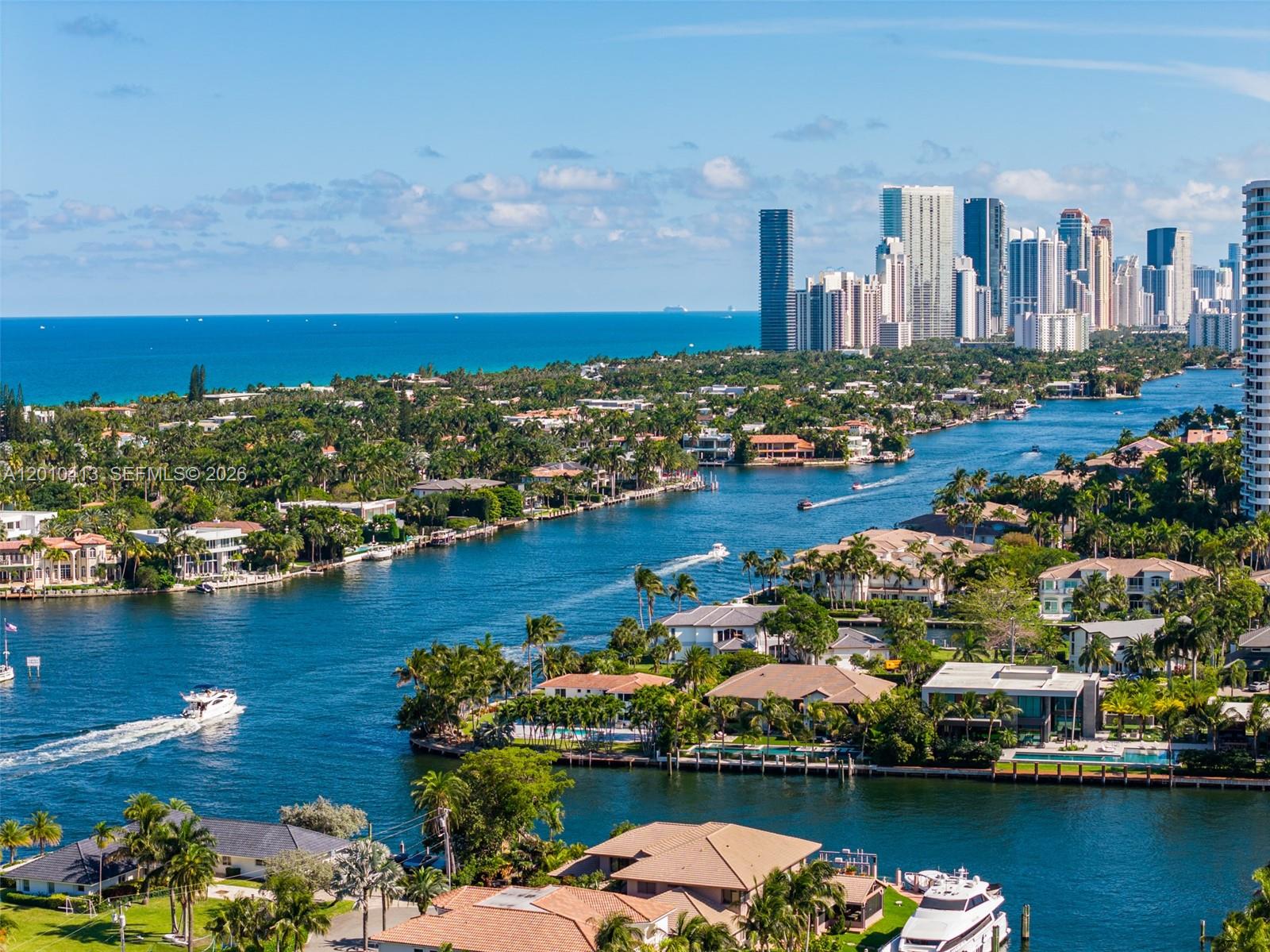 An aerial view shows a waterway winding through a residential area toward a coastal city skyline — 110 Holiday Dr, Hallandale Beach FL 33009, HALLANDALE BEACH, FL